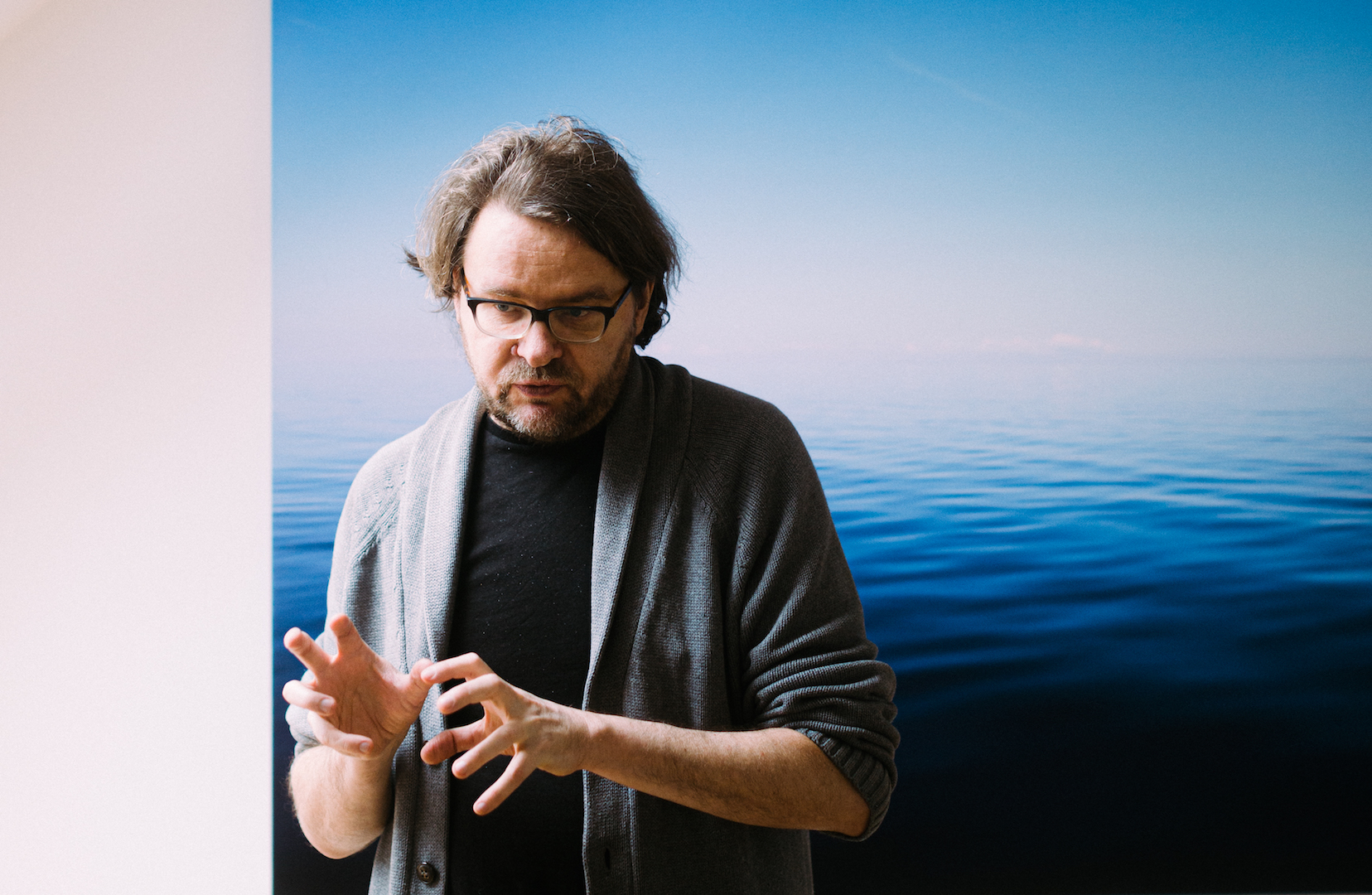 Kirjanik Jan Kaus oma kodus seismas Arne Maasiku suuremõõdulise merefoto ees .